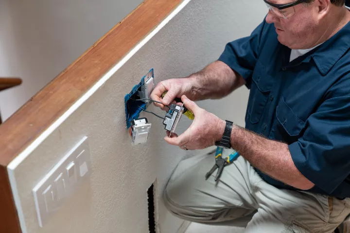 An electrician wearing a blue shirt works on repairing a socket.