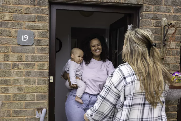 Woman with baby chatting to another woman at front door of house