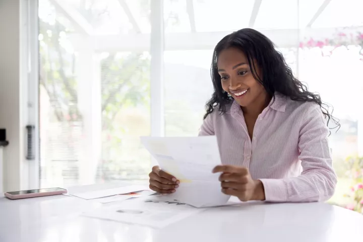 A young black woman with long hair smiles as she reads an official letter.