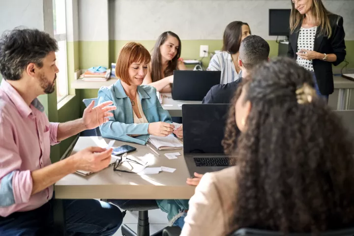 Room of people sitting in groups around a laptop in discussions