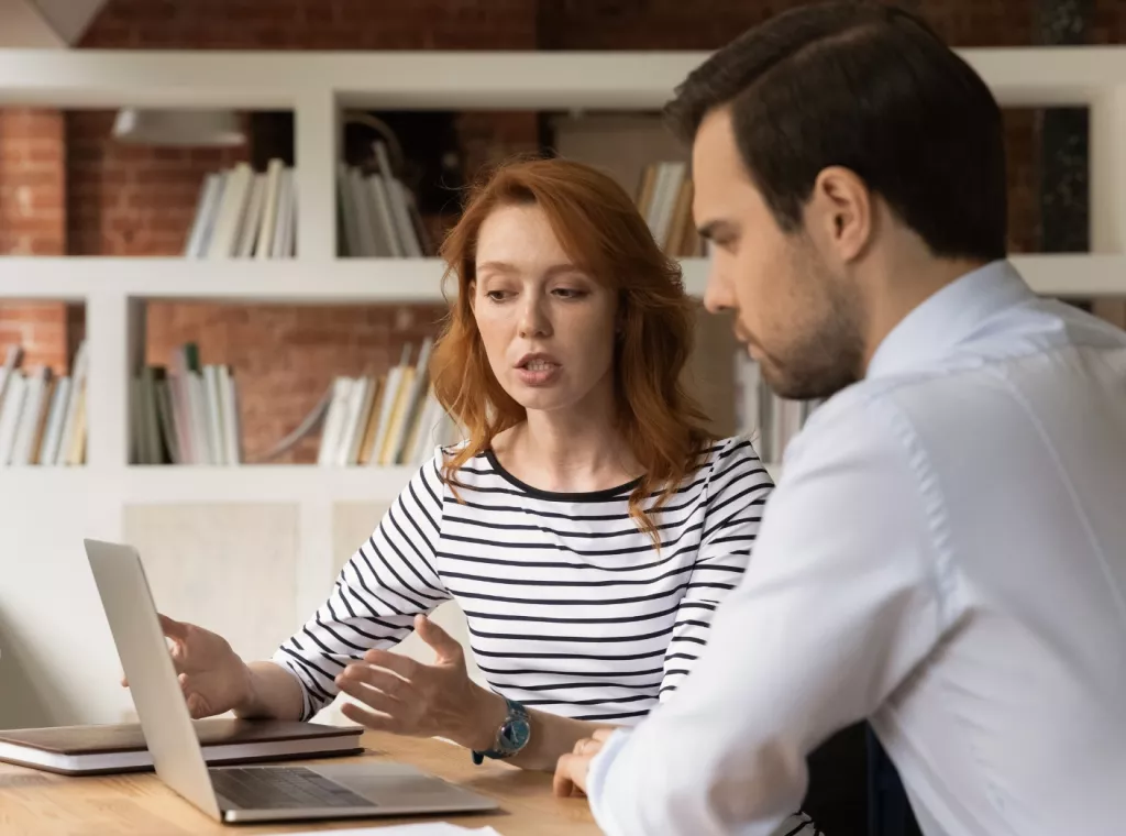 A man and woman in discussion at a desk with laptop